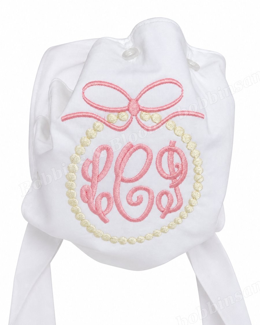 White baby bonnet embroidered with a pink bow and monogram, with ties