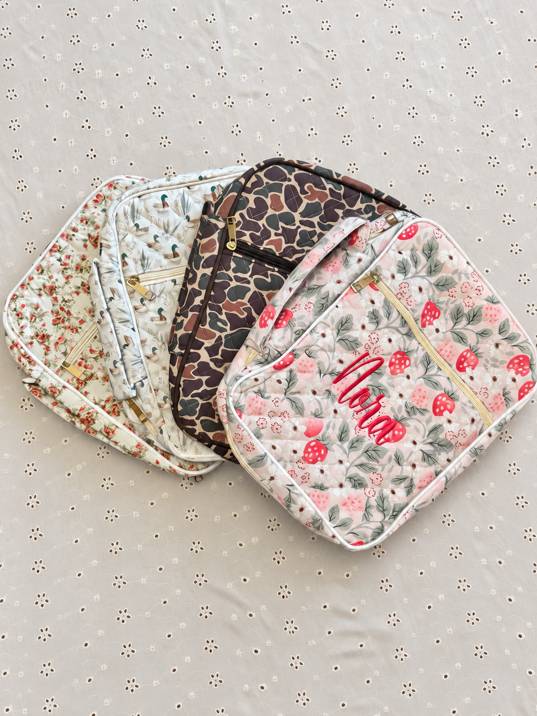 Four embroidered Bible covers in floral, mallard duck, camo, and strawberry patterns, one monogrammed with the name Nora