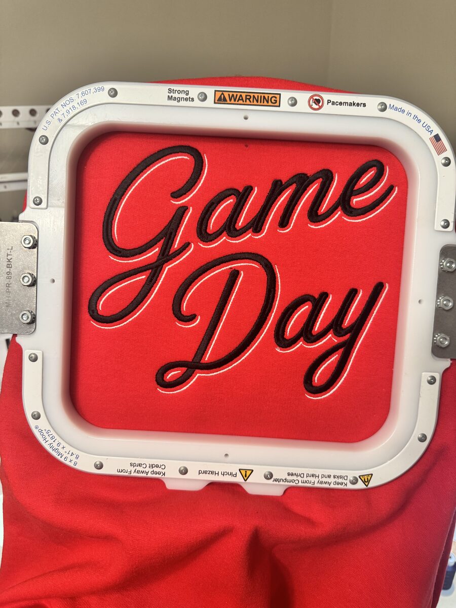 Red shirt embroidered with 'Game Day' in black script lettering with a white outline