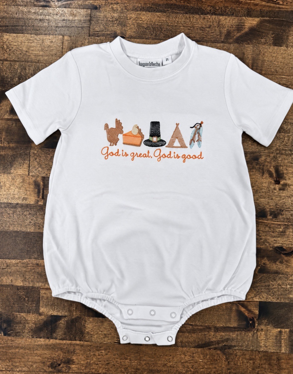 White kids bubble romper embroidered with a turkey, pie slice, pilgrim hat, teepee, and feather, with the words God is great, God is good