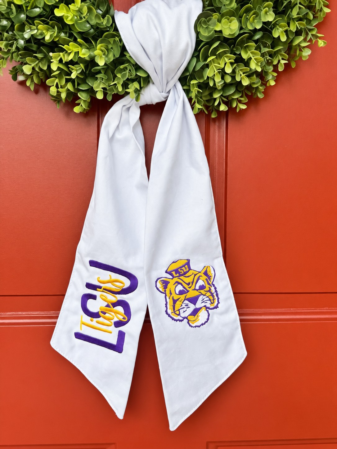 White wreath sash embroidered with LSU Tigers logo and tiger mascot, tied to a boxwood wreath on a red door