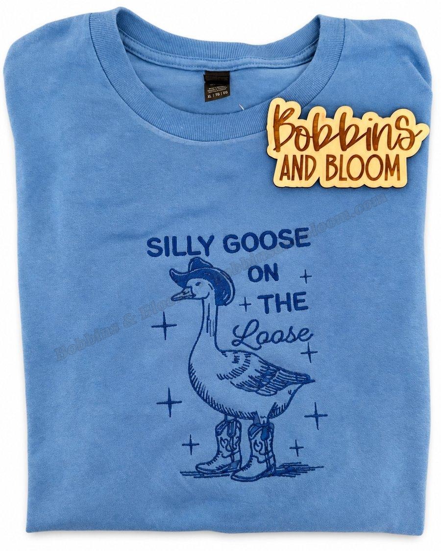 Blue sweatshirt embroidered with a goose wearing a cowboy hat and boots, and the words Silly Goose on the Loose