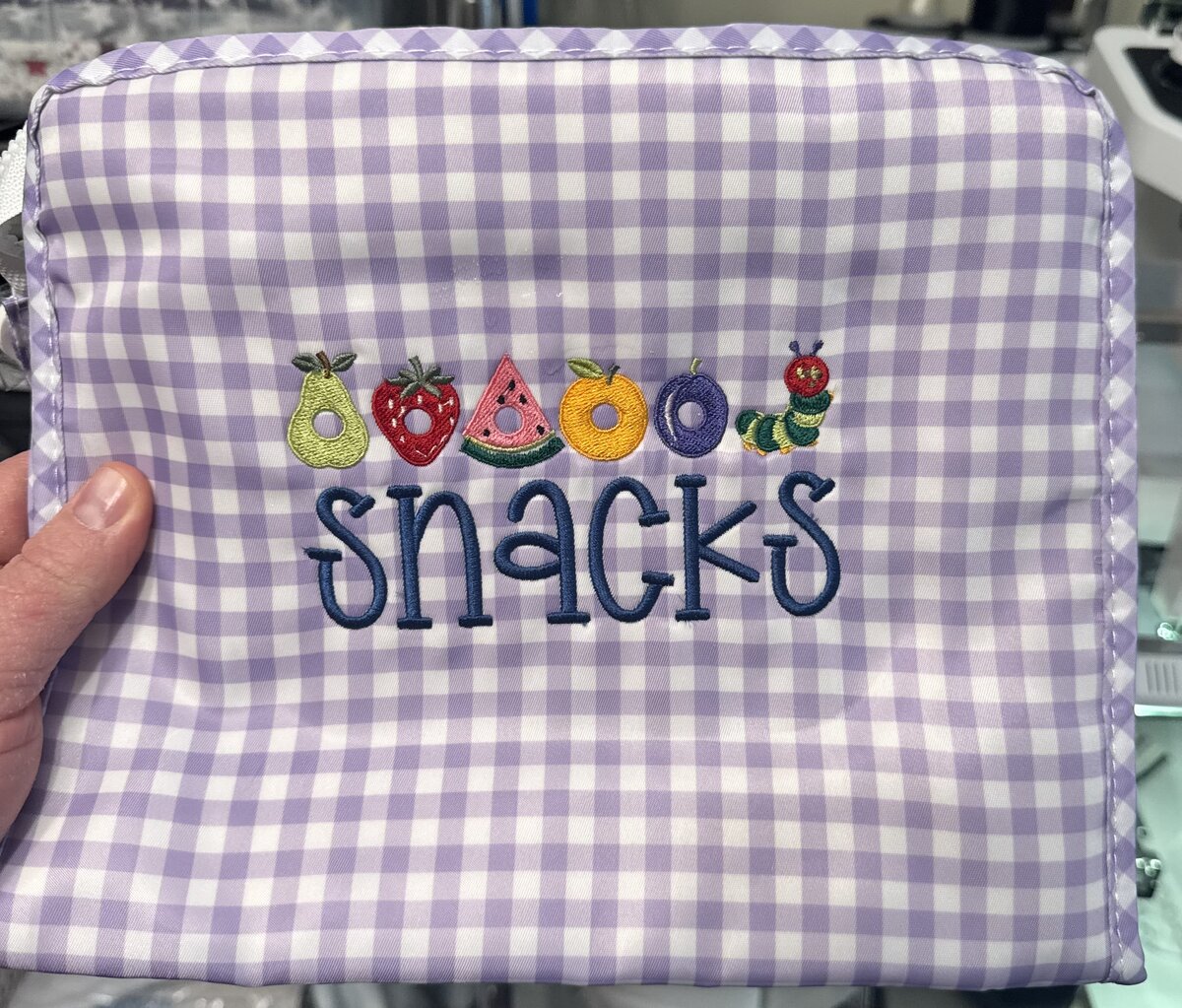 Finished Snack Pouch in purple gingham with a pear, strawberry, watermelon, orange, plum, and caterpillar design embroidered above the word snacks
